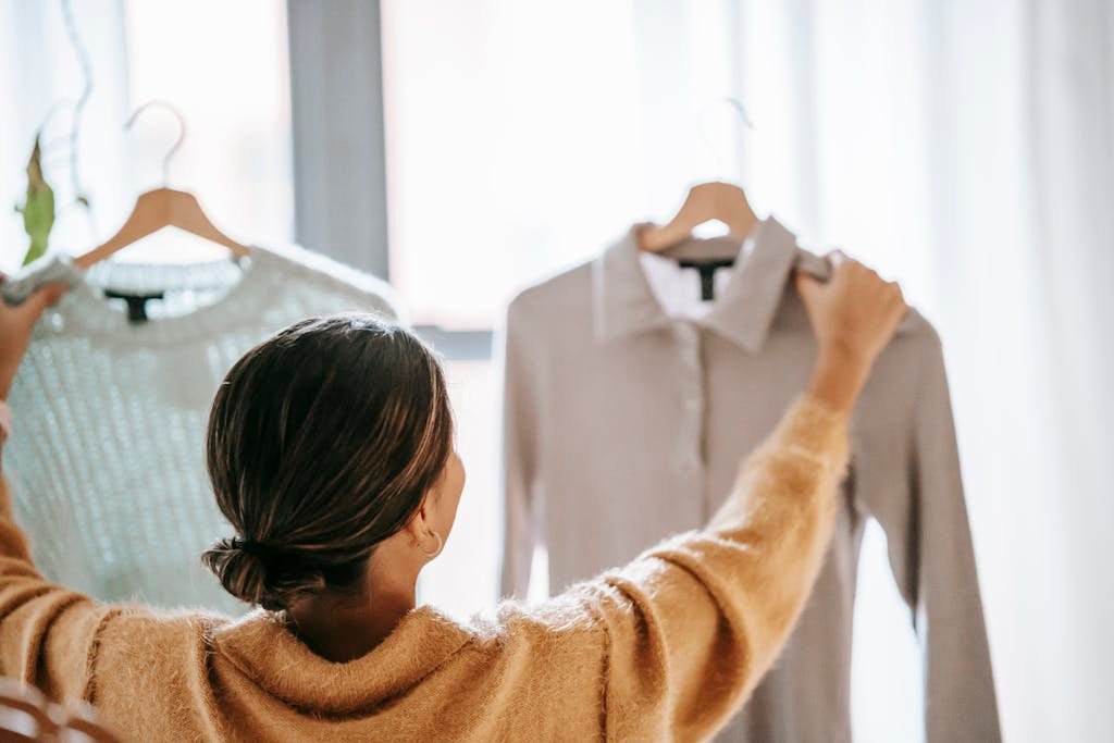 Una mujer decidiendo entre dos elegantes conjuntos en un acogedor ambiente boutique.